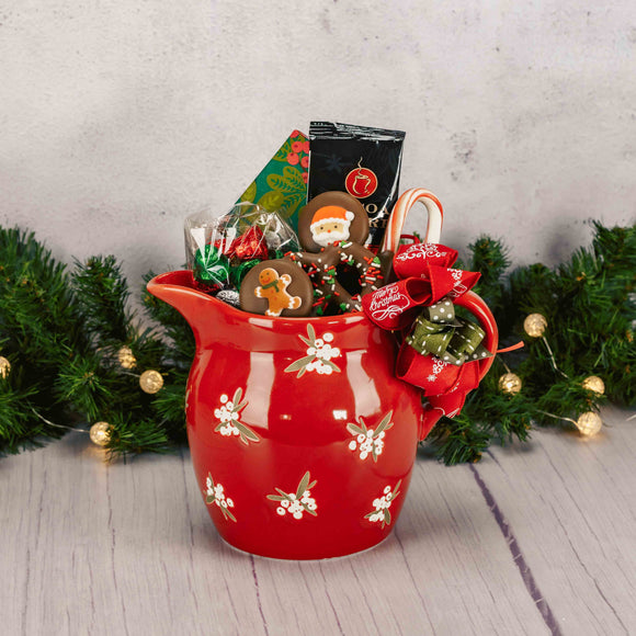 a red ceramic pitcher with winter berries on it is filled with candy and treats