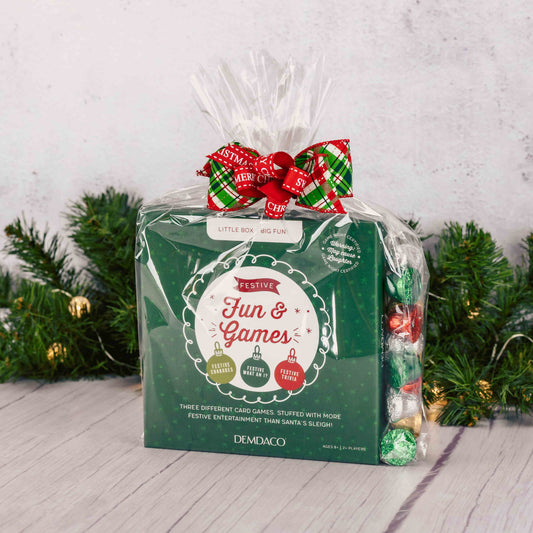 Gift set with festive card games and candy, wrapped in green packaging with a red bow.