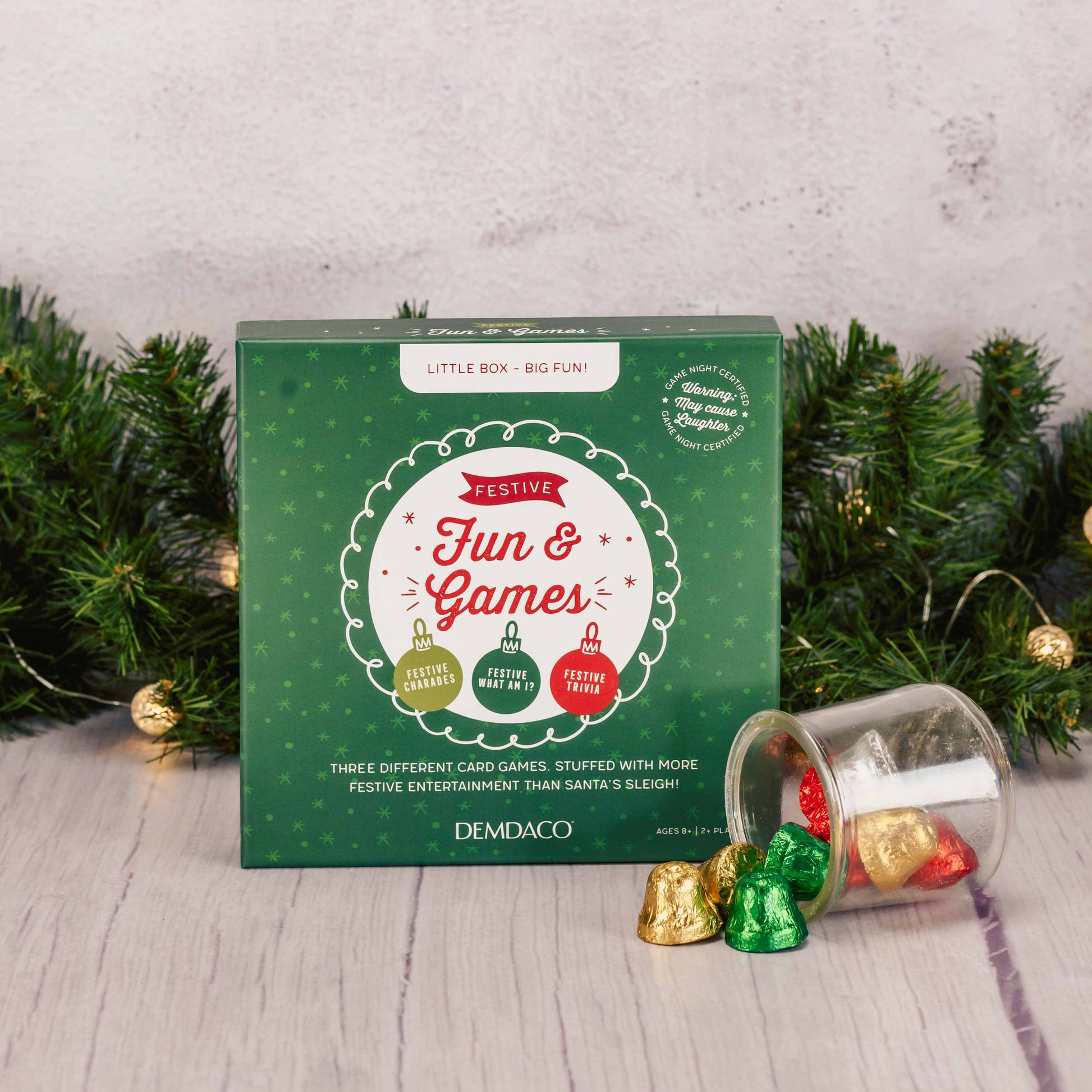 Gift set with festive card games and candy, wrapped in green packaging with a red bow.