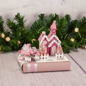 a half pound box of assorted chocolates is topped with a lighted pink house ornament