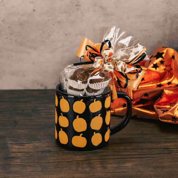 a black mug with orange pumpkins all over is filled with over a half pound of assorted milk chocolates