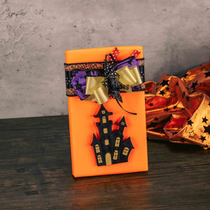 one pound box of assorted chocolates is wrapped in neon orange and topped with a black haunted house resin ornament