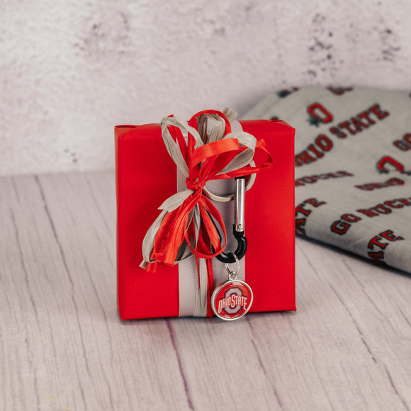 a sampler box of assorted chocolates is topped with an Ohio State carabiner keychain with a charm
