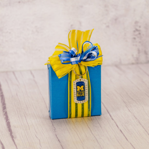  a sampler box of assorted chocolates is wrapped and topped with a dog tag styled Michigan keychain that reads 'Let's go blue' and has crystals around the edge