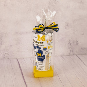 a tall tumbler cup with lid and straw featuring all things Michigan football is packaged with some sweet treats