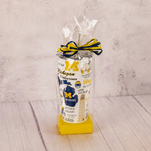 a tall tumbler cup with lid and straw featuring all things Michigan football is packaged with some sweet treats