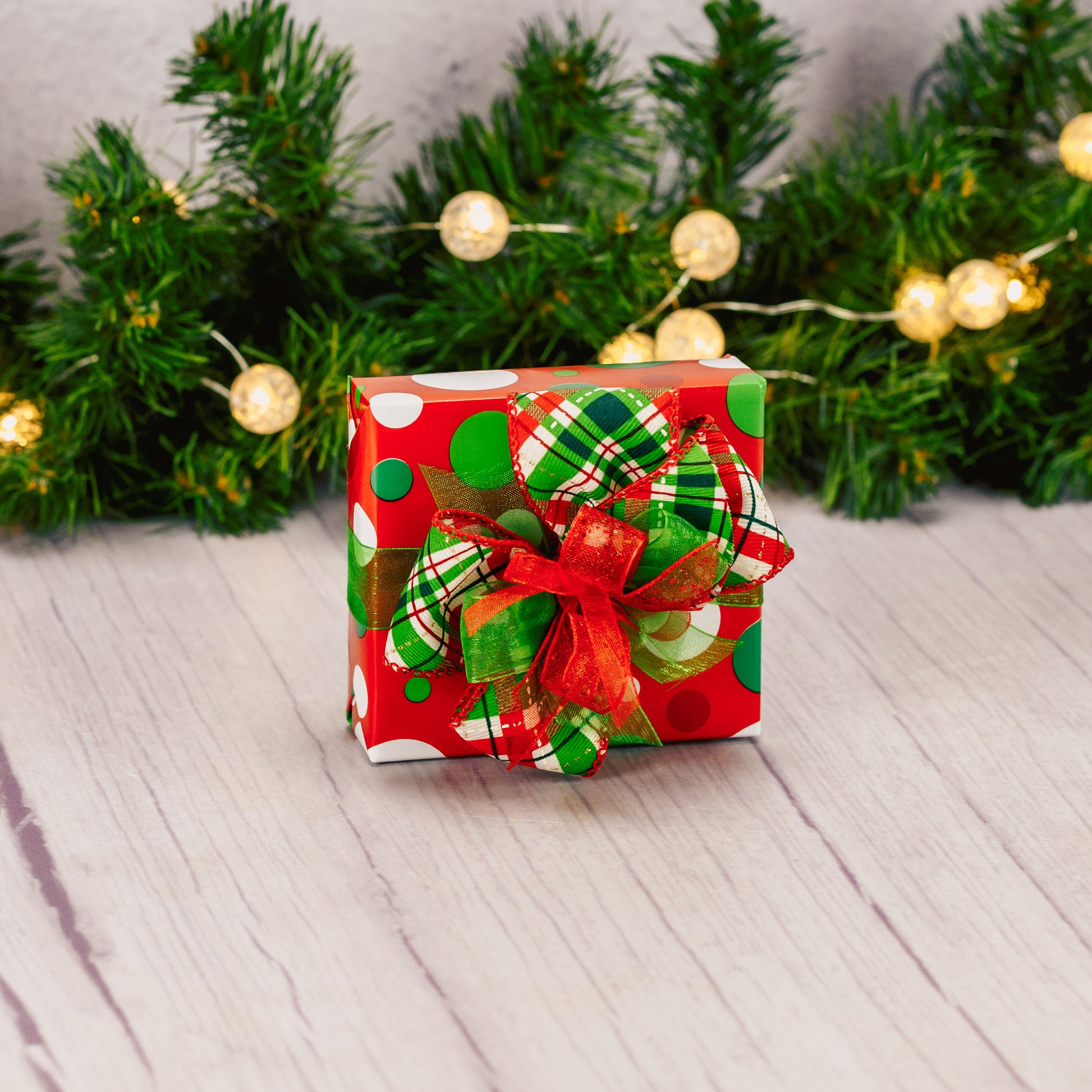 A sampler box of assorted chocolates is wrapped in festive Christmas colored polka dot paper and tied with a handmade bow