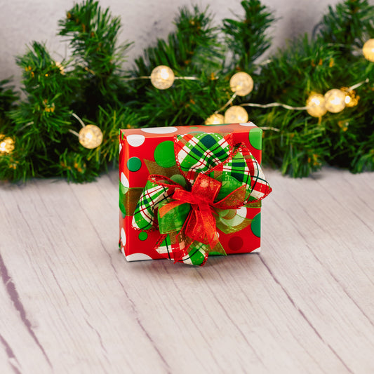 A sampler box of assorted chocolates is wrapped in festive Christmas colored polka dot paper and tied with a handmade bow