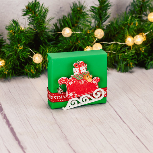 a sampler box of assorted chocolates is wrapped in green and topped with a wooden sleigh ornament