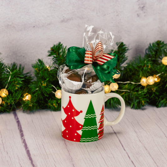 a festive mug that features red and green trees all around the mug is filled with a half pound of our assorted milk chocolates