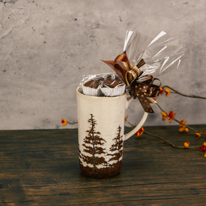 a tall mug with pine trees all around is filled with a half pound of our assorted chocolates