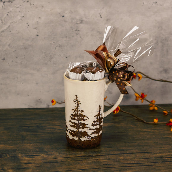 a tall mug with pine trees all around is filled with a half pound of our assorted chocolates
