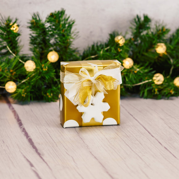 a sampler box of assorted chocolates is wrapped in gold and white polka dot paper and topped with a ceramic snowflake ornament made locally from individuals from RTC services programs.
