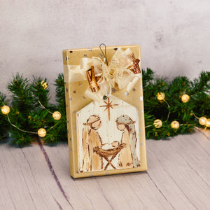 a one pound box of assorted chocolates is wrapped and topped with a wooden nativity ornament
