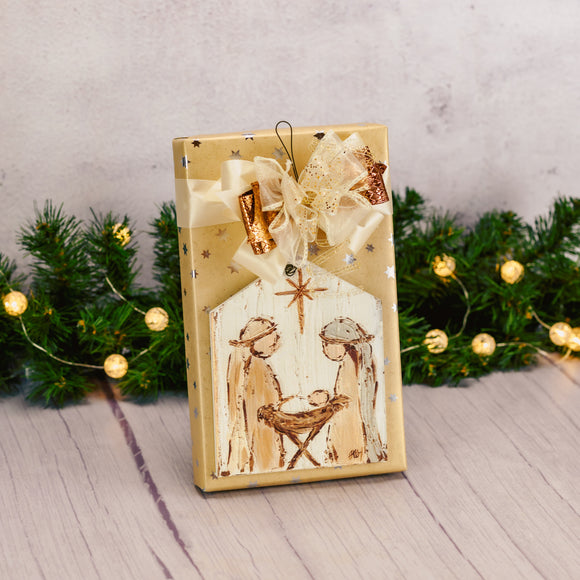 a one pound box of assorted chocolates is wrapped and topped with a wooden nativity ornament