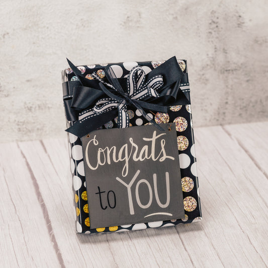 a half pound of our assorted chocolates wrapped and tied with a handmade bow and topped with a wooden plaque that reads 'congrats to you'