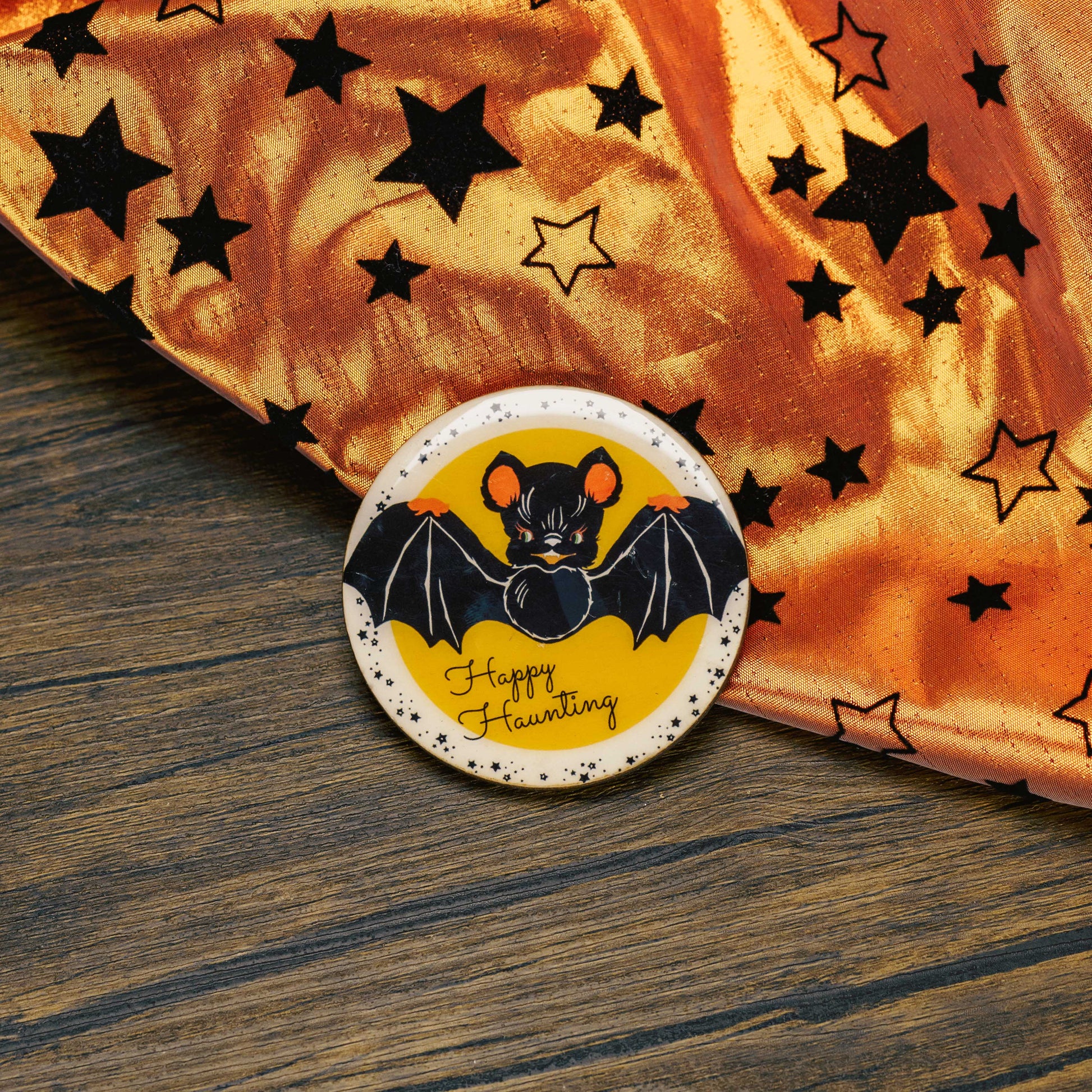 a round wooden bat Halloween magnet, that reads 'happy haunting' is placed on a sampler box of assorted chocolates.
