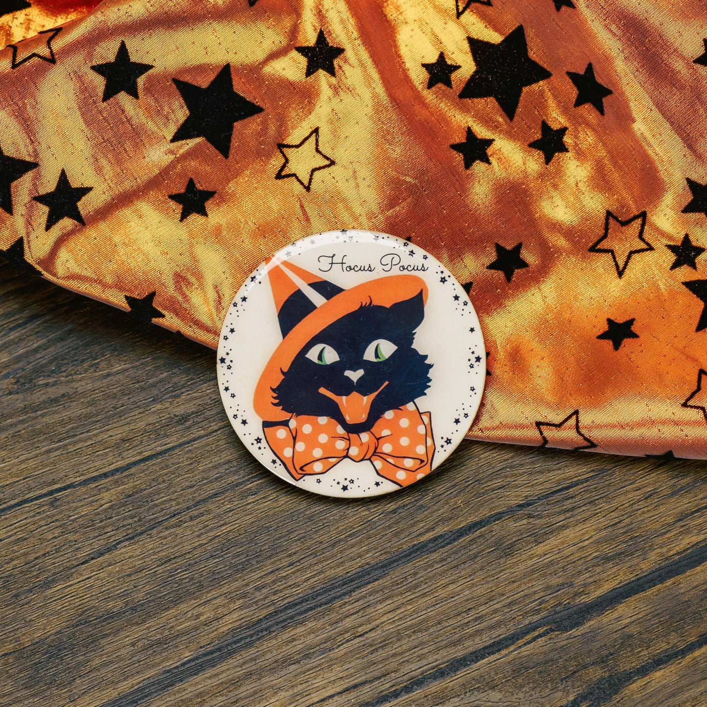 a round wooden cat Halloween magnet that reads, hocus pocus, is placed on a sampler box of assorted chocolates.