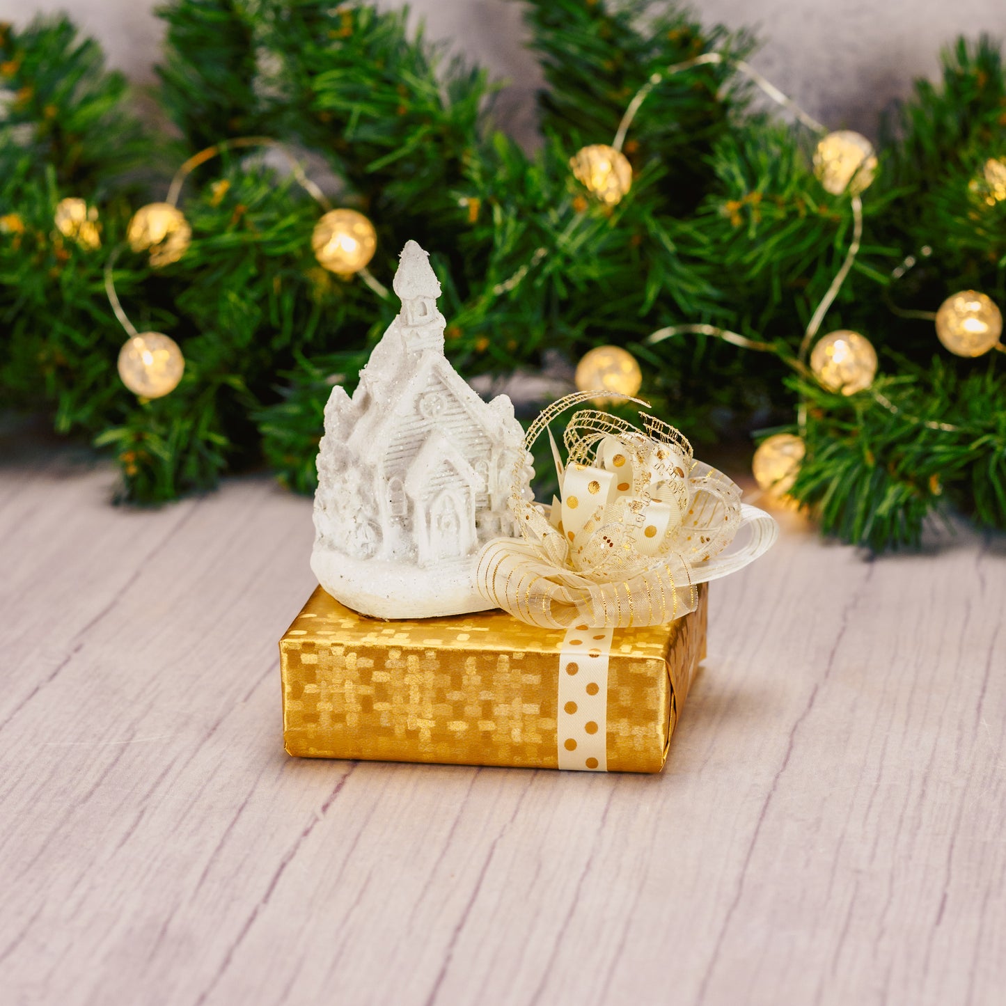 a white resin LED church figurine is placed on top of a sampler box of assorted chocolates.