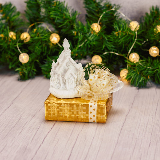 a white resin LED church figurine is placed on top of a sampler box of assorted chocolates.