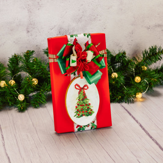 a one pound box of assorted chocolates is wrapped in red and topped with a wooden and painted tree ornament