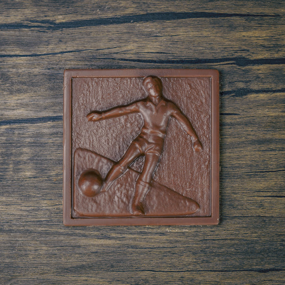 a square plaque of a soccer player kicking the ball in smooth milk chocolate