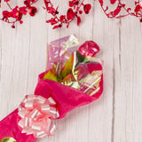 long stem milk chocolate rose wrapped in pink foil placed in tissue paper and tied with a bow.