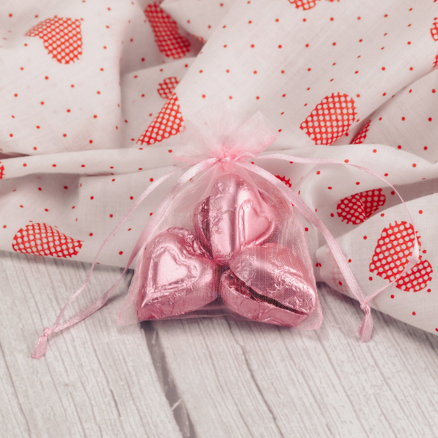 six milk chocolate foil wrapped hearts are placed in a pink gauzy pouch.