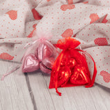six milk chocolate foil wrapped hearts are placed in a red or pink gauzy pouch.