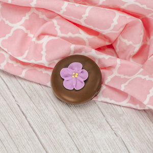 A crunchy Oreo cookie dipped in smooth milk chocolate or rich white coating with a sugar flower decoration on top.