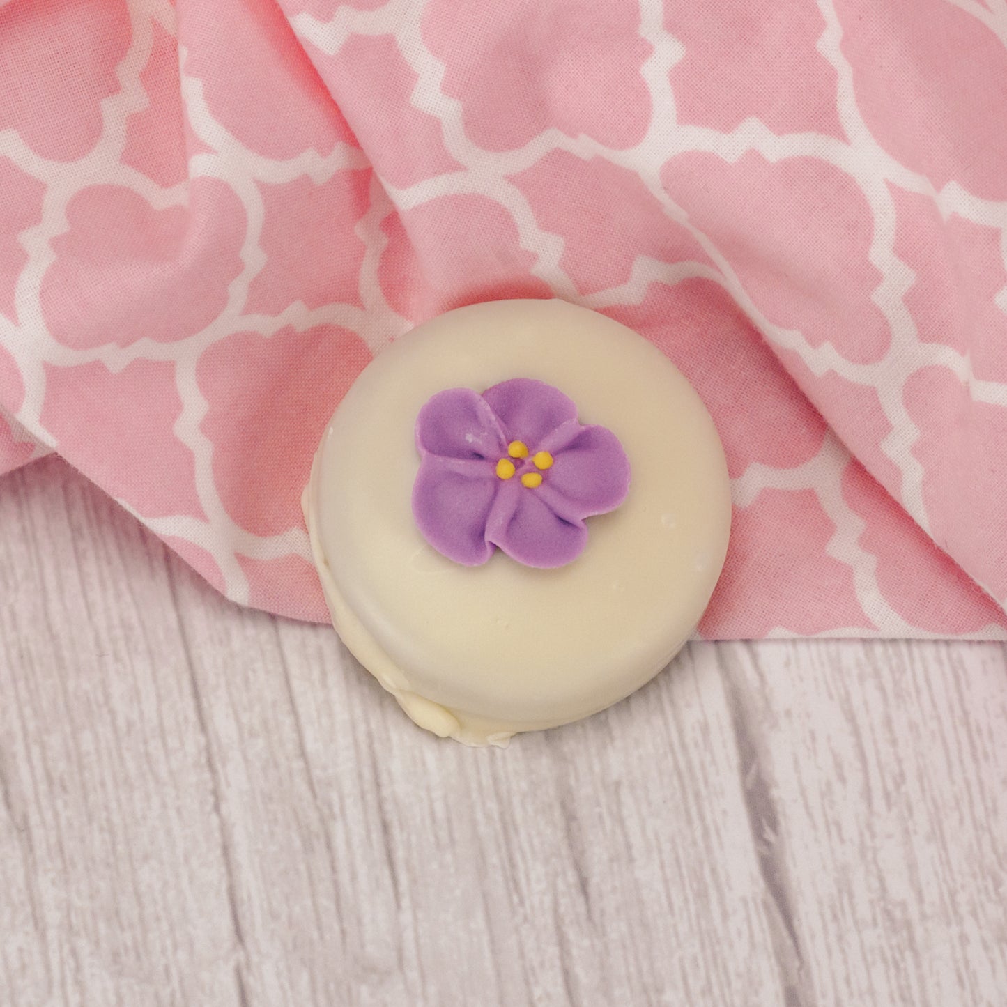 A crunchy Oreo cookie dipped in rich white coating with a sugar flower decoration on top.