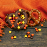 A jumbo pretzel covered in milk chocolate with mini Reese's Pieces sprinkled on top.