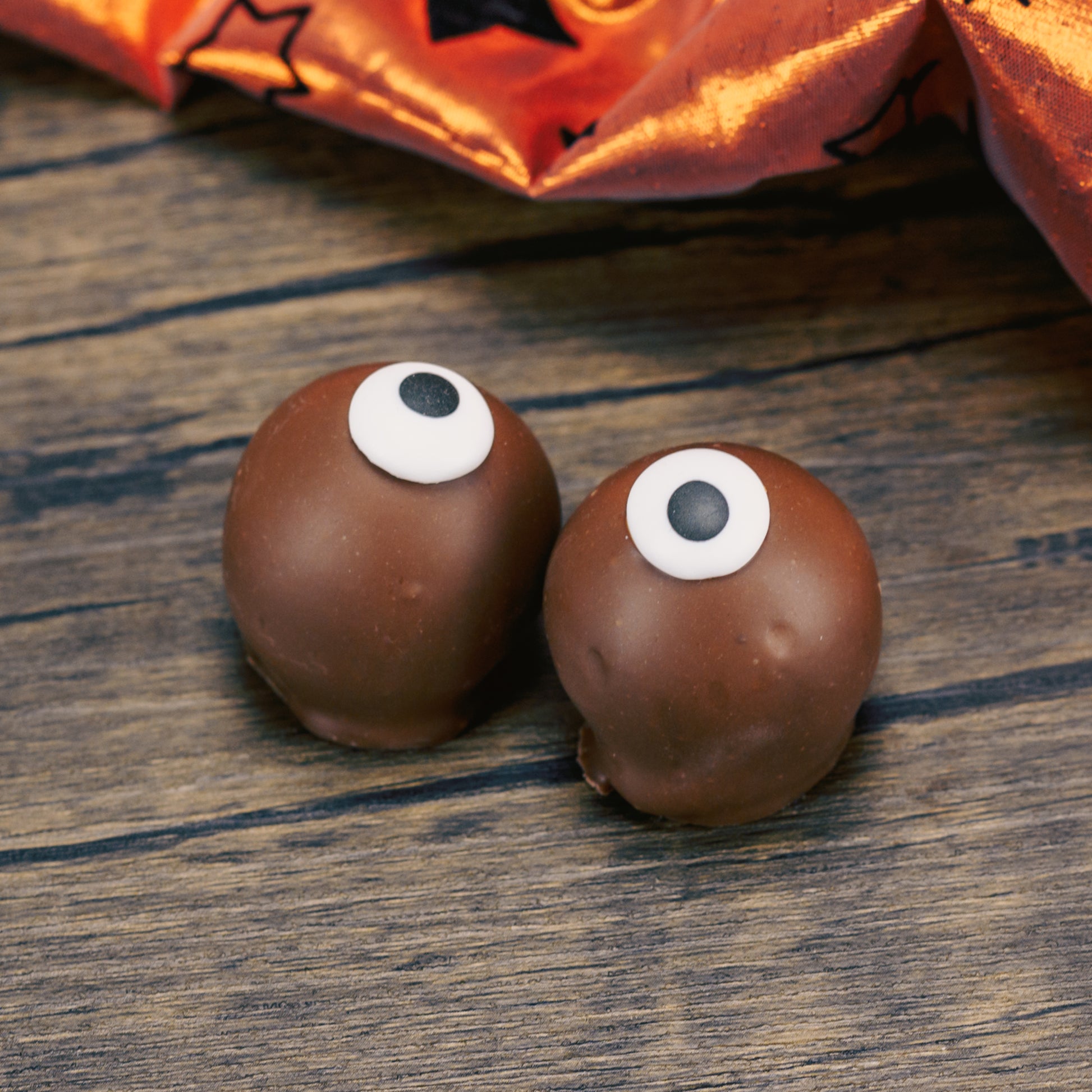 Two milk chocolate malt balls covered in milk chocolate. Each has an icing eye on it.
