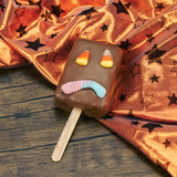 A rectangle Rice Krispie Treat on a stick covered in milk chocolate with a sour neon worm for a mouth and candy corn for eyes.
