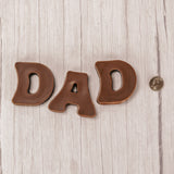 Milk chocolate letters spell out D.A.D and are placed in a box with a clear lid.