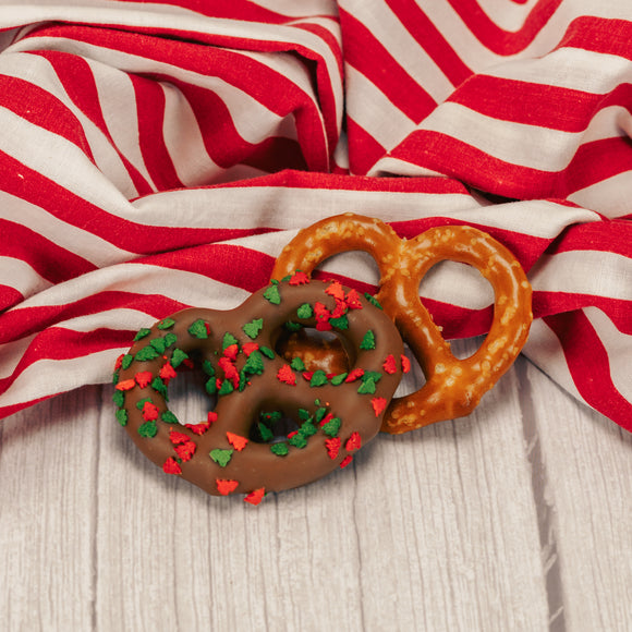 A jumbo pretzel covered in smooth milk chocolate sprinkled with red and green treess.